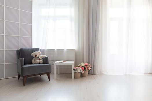 Armchair with toy book and flowers in the interior of a white room with a window