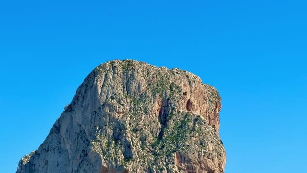 This breathtaking shot captures a steep rock face towering above a crystalclear sea beneath a vibrant blue sky