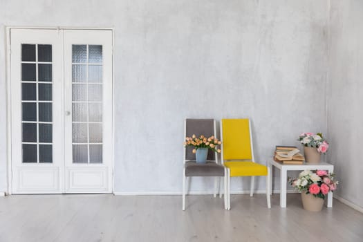 two chairs and a table with books and flowers in the interior of a white room