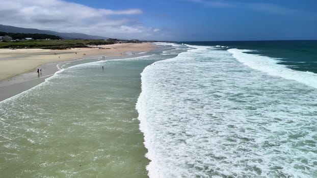 A stunning aerial view showcases a peaceful beach featuring rolling waves along the sandy shores, creating beauty