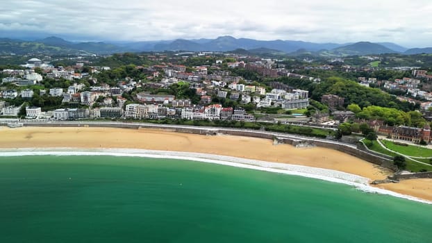 The aerial view showcases a beautiful beach and coastal town with vibrant blue waters and soft, sandy shores
