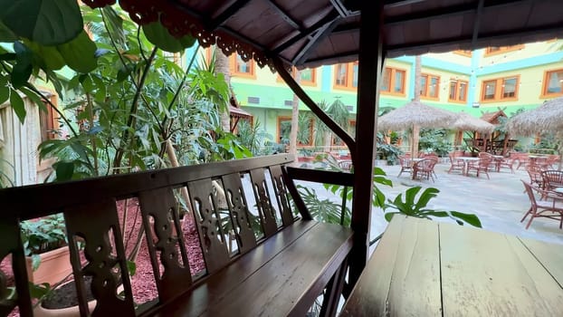 An inviting outdoor seating area features stylish wooden furniture amidst vibrant greenery at a charming restaurant