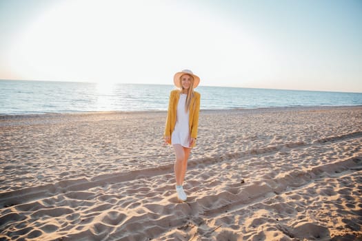 Beautiful blonde woman in summer dress walking on the beach by the sea