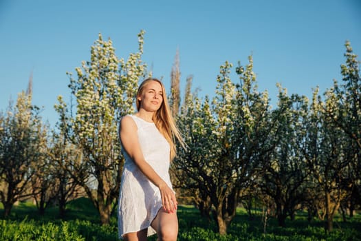 Blonde woman in summer dress walking in blooming garden in spring