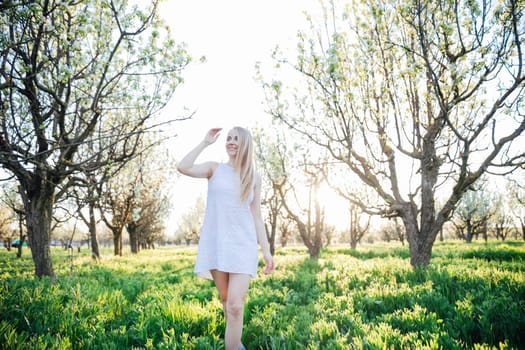 Blonde woman in summer dress walking in blooming garden in spring