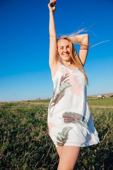 Woman in summer dress laughing and running on green field at sunset