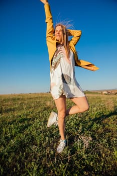 Woman in summer dress laughing and running on green field at sunset