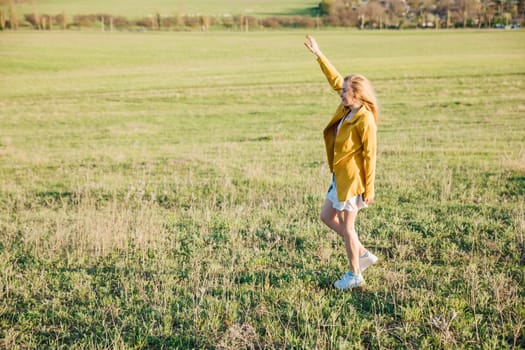 Woman in summer dress laughing and running on green field at sunset