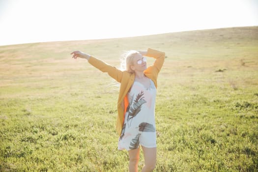 Woman in summer dress laughing at sunset on green field