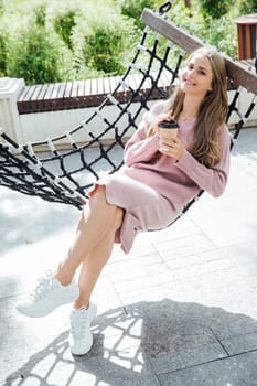 Blonde woman in pink dress on a swing with a cup of cocktail coffee