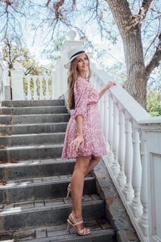 Blonde woman in summer pink dress and hat on street smiling
