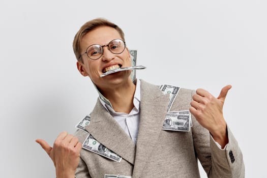 Cheerful man wearing glasses and a beige suit decorated with dollar bills, smiling widely while holding a toothbrush in his mouth and giving thumbs up, against a clean white backdrop. Concept: humor, money, business casual, playful attitude, financial success.