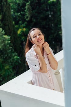 Brunette woman in summer pink dress on the balcony of the house smiling