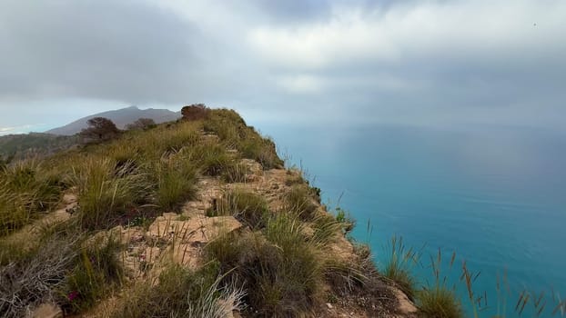 Venture out to explore the breathtakingly dramatic coastal cliffs alongside the serene azure ocean beneath cloudy skies