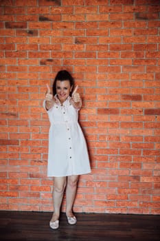The brunette has given a thumbs up and is smiling at the brick wall