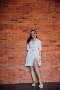 Brunette woman in light summer dress smiling at brick wall