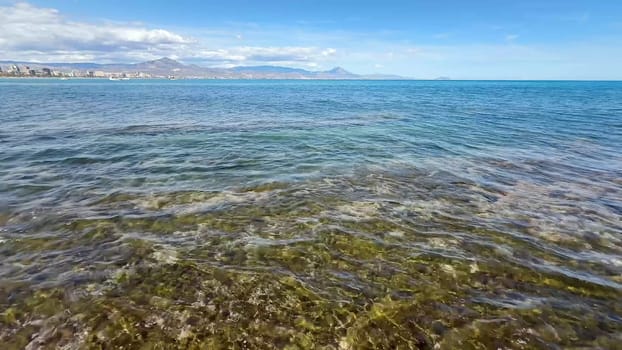 A serene and tranquil coastal scene showcasing crystal clear blue waters, rocky shores, and distant majestic mountains