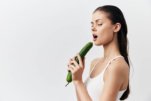 Young woman with wet hair and a confident expression holds a cucumber near her lips in a lighthearted manner The neutral white background emphasizes the playful concept of food and sensuality