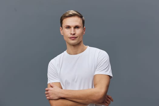 Young caucasian man wear white t-shirt look camera with neutral expression and arms crossed stand against plain gray background. The casual confident pose suggests mental health and digital detox from gadgets lifestyle concept.