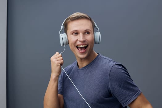 Happy young caucasian man wearing headphones listening to music looks excited and relaxed isolated on gray background showing joy and mental health through digital detox concept and casual style
