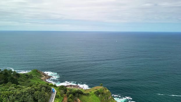 This stunning landscape beautifully features the vast ocean, lush rolling hills, and a peaceful coastal road