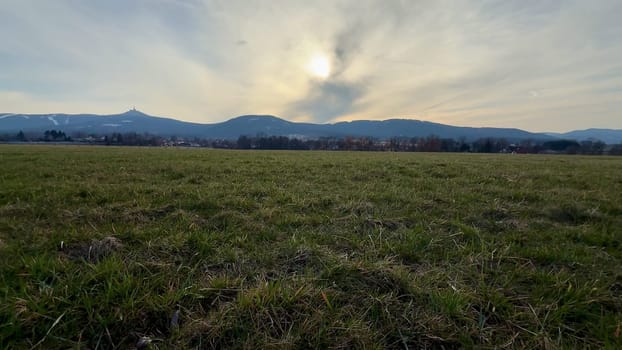 A stunningly peaceful landscape featuring majestic mountains, an open grassy field, and a tranquil dusk sky