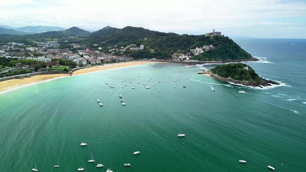 Aerial view of a picturesque beach, surrounded by lush hills, with boats bobbing in sparkling water