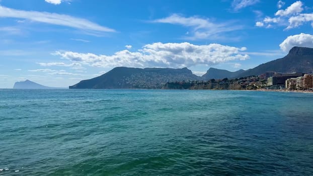 The stunning coastal scenery includes clear water, majestic mountains, and sandy beaches in the background