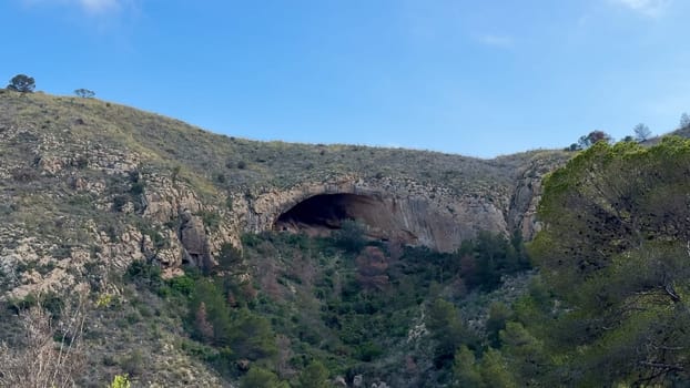 A captivating and breathtaking view of a cave, beautifully surrounded by lush greenery and majestic rocky hills