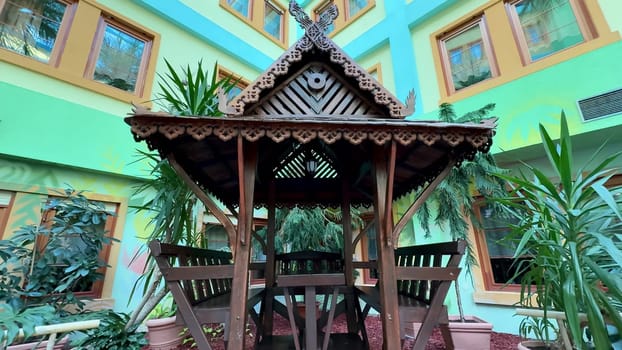 A beautifully designed and crafted wooden gazebo is perfectly nestled among the vibrant greenery in a colorful setting