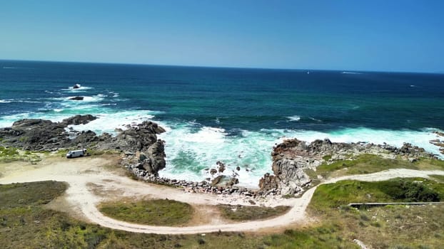 Experience stunning coastal views with roaring waves, rocky formations, and lush greenery under a clear blue sky