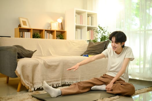 Young asian man stretching on a yoga mat in a cozy living room.