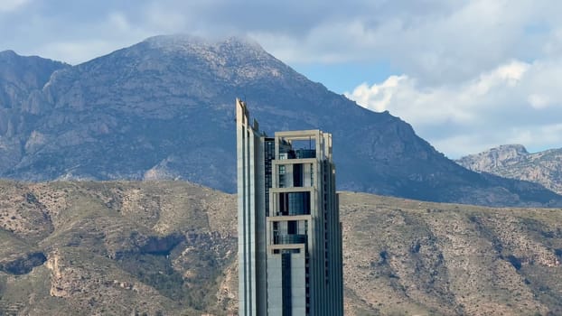A strikingly impressive skyscraper rises majestically above a picturesque and serene mountainous backdrop
