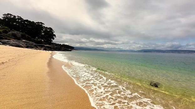 This serene beach scene showcases the soft sands and perfectly calm waters, all beneath a cloudy, overcast sky
