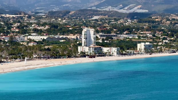 An aerial view shows a serene beach with clear turquoise waters and beautiful beachfront properties