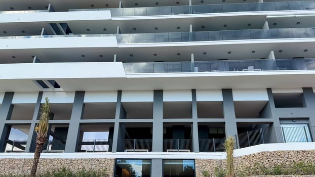 A modern multistory building showcases stylish curved balconies set against a bright and vivid blue sky