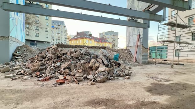 A construction site presents a large pile of rubble set against the backdrop of towering urban buildings nearby
