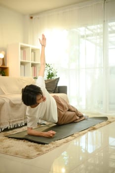 Young man doing a side plank exercise on a yoga mat in a living room.