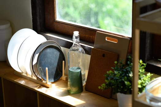 Minimalist kitchen scene with plates, glass bottle, and plant near a wooden window.