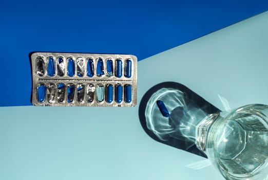 Medicine in blue capsules on a blue and light blue background. A glass of water and capsules in a blister. space for text