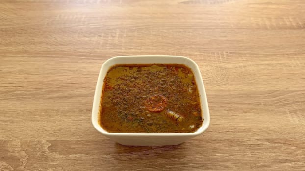 A vibrant and colorful herbal soup served in a pristine white bowl, finely presented on a rustic wooden surface