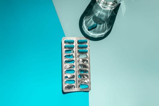 medicine in capsules and a glass of water on a blue background top view. Medical pharmacy concept. High quality photo