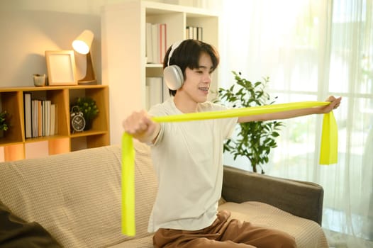 Smiling man in headphones working out with resistance band in a living room.