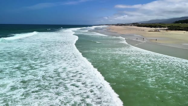 Stunning aerial view showcasing the mesmerizing waves crashing upon a sandy beach beneath a pristine, clear blue sky