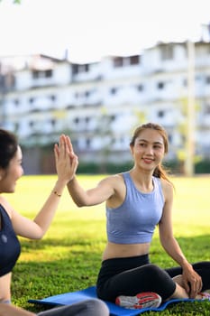 Two happy women giving a high five after successful outdoor workout session on mats.