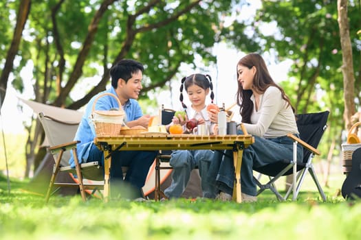 Happy family enjoying breakfast at a table while camping in a forest park.