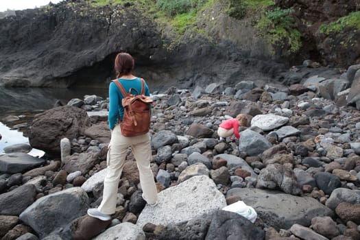 Tourist with leather backpack exploring rocky coastline with her daughter