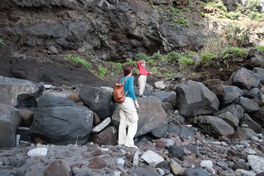 Mother and son exploring a rocky volcanic landscape, enjoying a hike amidst nature's rugged beauty