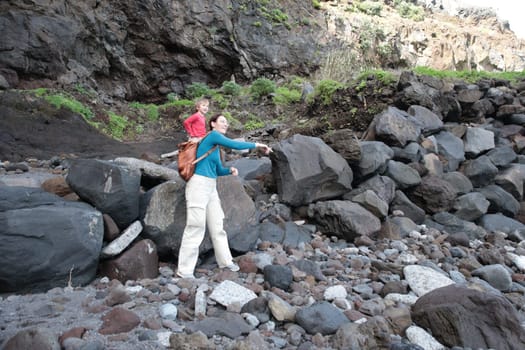 Woman pointing to something while hiking with her child on a rocky beach