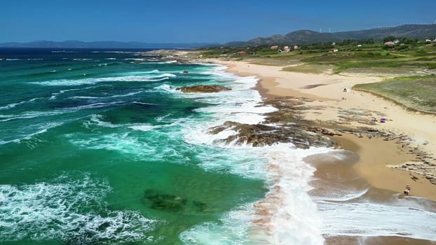 Experience a breathtaking aerial view of waves crashing on a sandy beach with lush greenery in the background